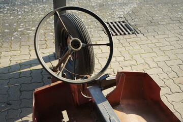 Lenkrad mit drei Speichen eines selbsgebauten vergammelten Dreirad auf Verbundpflaster im...