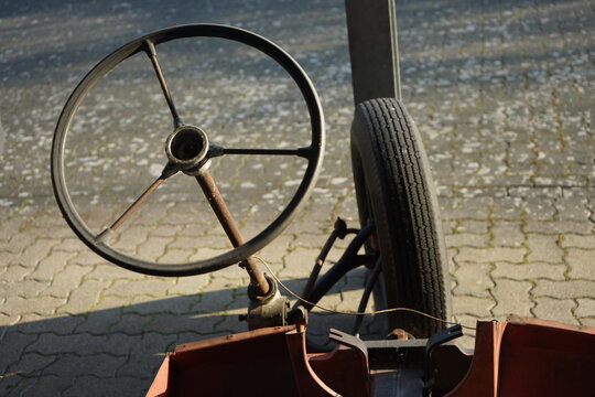 Lenkrad mit drei Speichen eines selbsgebauten vergammelten Dreirad auf Verbundpflaster im Sonnenschein am Automuseum in Lemgo Hörstmar bei Detmold in Ostwestfalen-Lippe