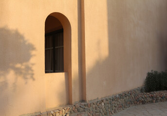 An arch window in the wall of the arabic building. Summer floral shadows on the wall. - 494560593
