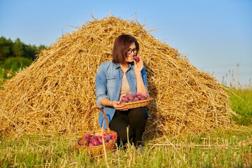 Naklejka na ściany i meble Summer rural woman portrait with basket of plums, dry hay sky background