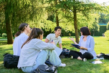 Group of high school students with female teacher, on campus lawn
