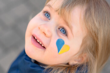 portrait of a girl with a blue and yellow heart on the cheek  - obrazy, fototapety, plakaty