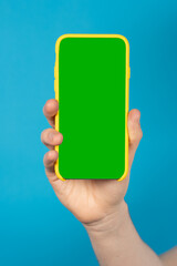 Green chroma on phone screen. Hand holding colorful smartphone on blue background