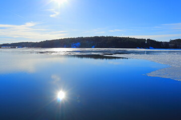 Sun reflection in the cold blue water. Swedish Mars or spring weather outside. Calm, clear lake with melting ice. Mälaren, Stockholm, Sweden, Scandinavia, Europe.