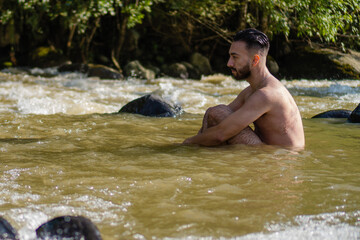 young latin man inside the river naked meditating, connecting with nature, with the environment