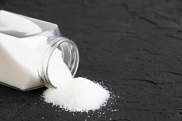 Glass jar with sugar black background.Diabetes. Scattered white sugar on a black table. Copy space. Place for text.Extra calories