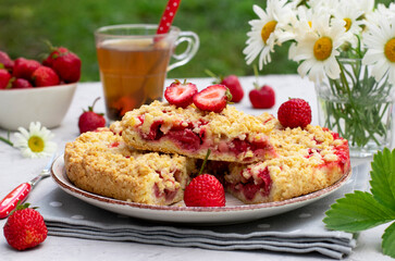 Italian sbricholata pie with shortcrust pastry and strawberries on light gray table with a bouquet of daisies