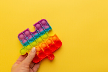 Colorful antistress sensory toys fidget push pop-it in girl's hand on yellow background
