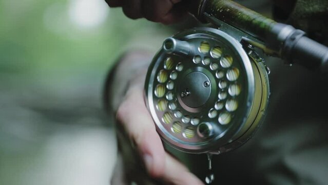 Fisherman is holding rod and line spool in hands. Water drops slowly dripping down and starts splashing when fishing reel starts to spin.