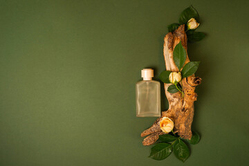 perfume bottle with wood and flowers roses on green background, copy space 