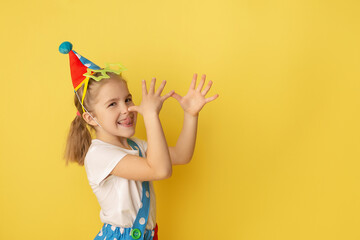 Funny kid clown against yellow background. Happy child playing with festive decor. Birthday and 1...