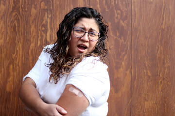 Fototapeta na wymiar Latin young adult woman with glasses and overweight shows her arm with bandage recently vaccinated against Covid-19 in the new normality of Coronavirus 