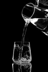 water pours into a glass from a decanter on black background