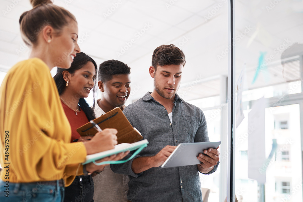 Poster Churning out great ideas with the smartest tools. Shot of a group of businesspeople using a digital tablet while brainstorming on a glass wall in an office.