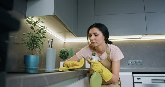 Young Housewife In Yellow Rubber Gloves Washes, Sprays And Wipes The Electric Stove On The Kitchen Counter With A Wet Yellow Rag With Detergent. Home Kitchen Cleaning Concept