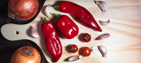 Closeup of wooden board with red pepper, garlic cloves and cherry tomatoes.