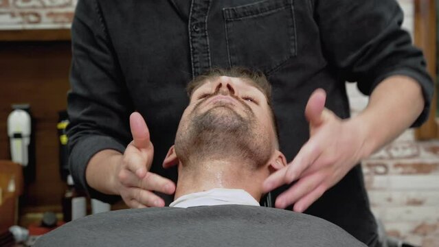 Hairdresser massaging and rubbing oil in young man's beard after giving him a haircut in professional barber shop. High quality 4k footage