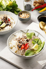 Pho Bo vietnamese soup with beef, rice noodles, pak choi and mushrooms in a grey bowl on marble board, peanuts, soy sauce, chilli