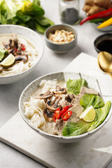 Pho Bo vietnamese soup with beef, rice noodles, pak choi and mushrooms in a grey bowl on marble board, peanuts, soy sauce, chilli