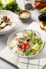 Pho Bo vietnamese soup with beef, rice noodles, pak choi and mushrooms in a grey bowl on marble board, peanuts, soy sauce, chilli