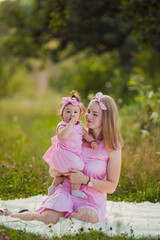 Obraz premium mother and daughter in pink dresses sit on a white blanket