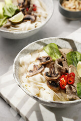 Pho Bo vietnamese soup with beef, rice noodles, pak choi and mushrooms in a grey bowl on marble board, peanuts, soy sauce, chilli