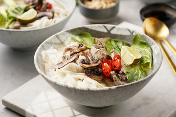 Pho Bo vietnamese soup with beef, rice noodles, pak choi and mushrooms in a grey bowl on marble...