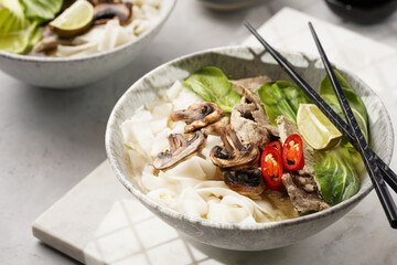 Pho Bo vietnamese soup with beef, rice noodles, pak choi and mushrooms in a grey bowl on marble board, peanuts, soy sauce, chilli