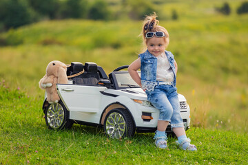 girl sits on the hood of a children's car that stands on the lawn