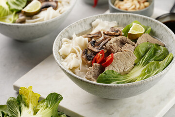 Pho Bo vietnamese soup with beef, rice noodles, pak choi and mushrooms in a grey bowl on marble...