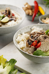 Pho Bo vietnamese soup with beef, rice noodles, pak choi and mushrooms in a grey bowl on marble board, peanuts, soy sauce, chilli