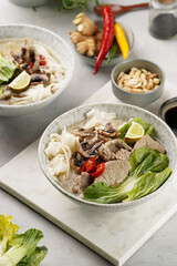Pho Bo vietnamese soup with beef, rice noodles, pak choi and mushrooms in a grey bowl on marble board, peanuts, soy sauce, chilli