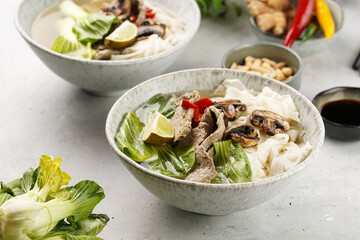 Pho Bo vietnamese soup with beef, rice noodles, pak choi and mushrooms in a grey bowl, peanuts, soy sauce, chilli