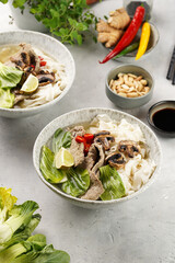 Pho Bo vietnamese soup with beef, rice noodles, pak choi and mushrooms in a grey bowl, peanuts, soy sauce, chilli