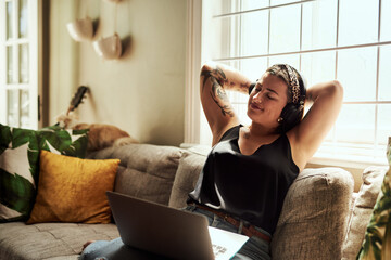 Good music washes the worries of the week away. Shot of a young woman using a laptop and headphones on the sofa at home. - Powered by Adobe