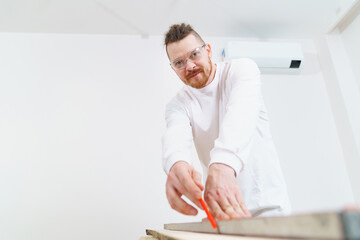 carpenter in protective glasses makes measurements and draws on wood