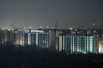 Dark silhouette of tower cranes at high residential apartment buildings construction site at night. Real estate development