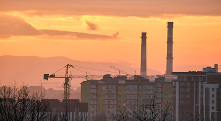 Fototapeta premium Dark silhouette of tower cranes at high residential apartment buildings construction site at sunset. Real estate development