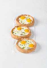 Mini rye cottage cheese open pies with mozzarella, quail eggs and dill, on paper. White background