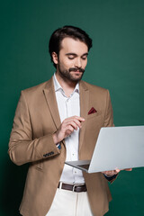 pleased young man with mustache using laptop on dark green.