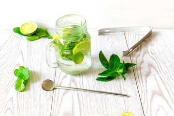 Fresh iced cold mojito lemonade summer drink, cocktail with sliced lime, bright green mint leaves and frozen ice cubes in a transparent cup, mason jar on wooden table