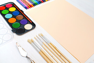 Watercolor oil paints, paintbrushes, colorful pencils, pastel crayons,blank watercolor paper pad. Creativity creation process. Artist's stuff on white table.Top view Flatlay of drawing supplies