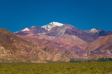 Snowy peak behind multicolored mountains in natural reserve El Leoncito, in the province of San Juan, Argentina.