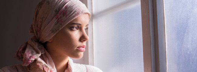 Young cancer patient standing in front of hospital window