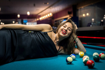 Beautiful lady lying on green snooker table among the balls