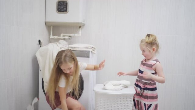two cute and cheerful girls play with laundry in the laundry room. 
