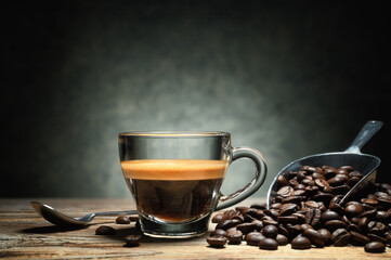 Steaming espresso in glass cup, with coffee beans on wooden table and gray background. Space for text.. - 494581140