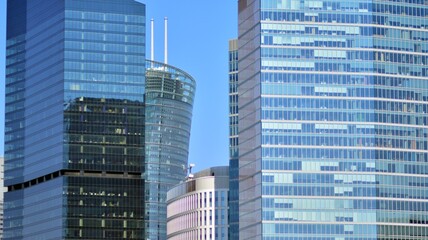 Obraz premium Minimalist glass facade, steel framework holding the large transparent panels. Contemporary commercial architecture, vertical converging geometric lines. Blue sky reflection in the glass panels