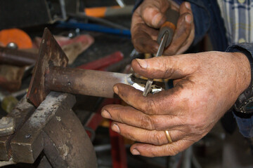 Dirty hands of an elderly blacksmith with a file while carrying out repair work in the workshop