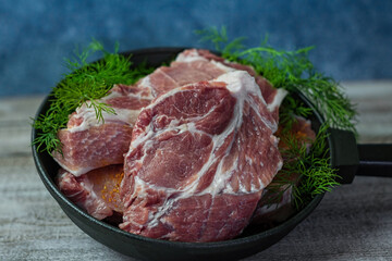 Close-up photo of cuts of meat with dill in a steak pan on wooden table with blue background